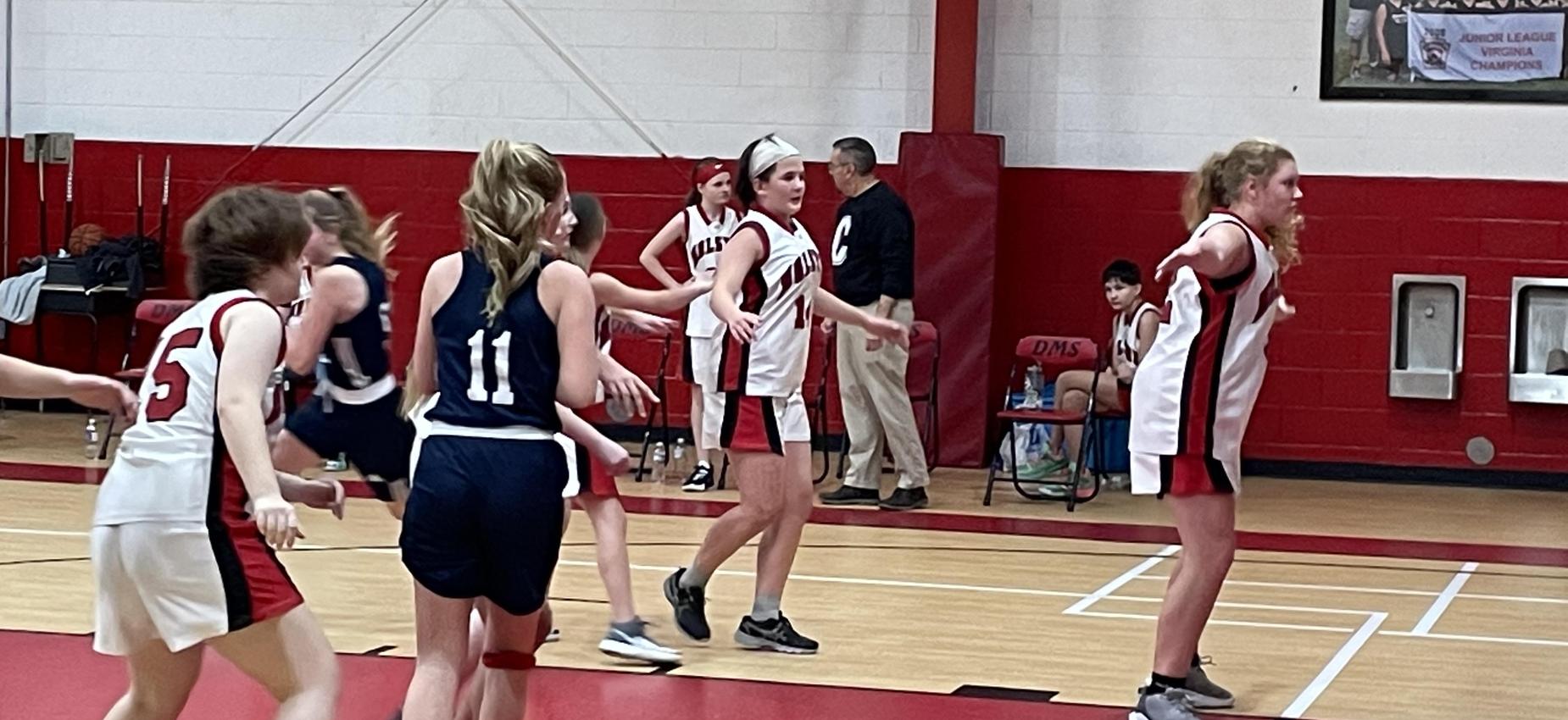 Girls play basketball in a gym.