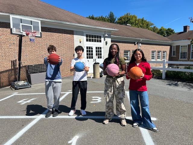 Four students on a playground holding basketballs