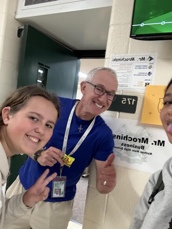 Smiling teacher poses with two students in a school hallway.