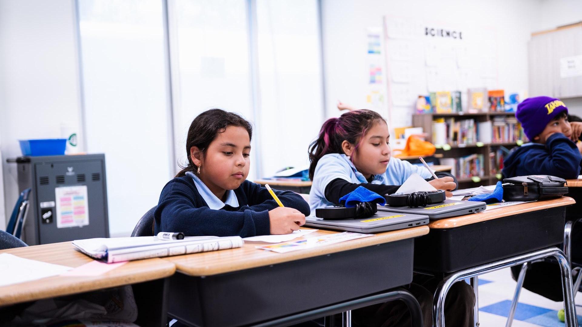 Children working at desks in a classroom, focused on their tasks.
