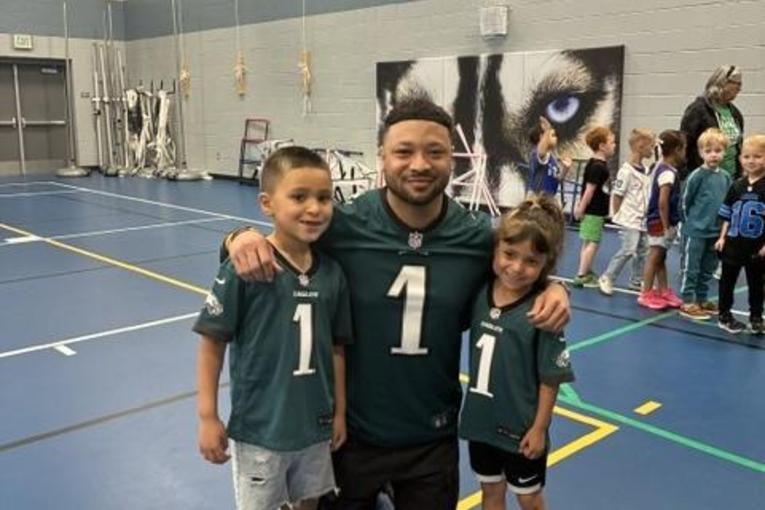 Three people, two children and an adult, wearing Eagles jerseys in a gymnasium.