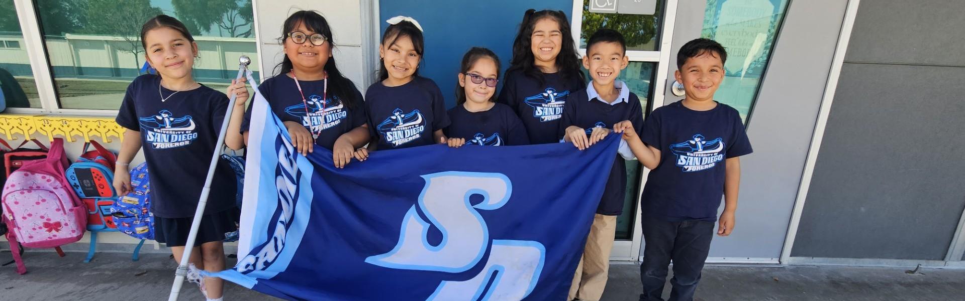 Group of students holding a blue flag with 'SD' on it, smiling together.