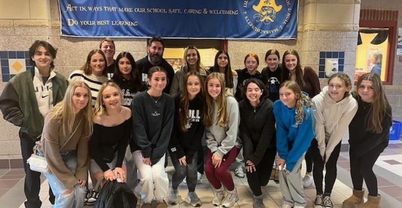 A group of students posing in front of a school banner with a teacher.