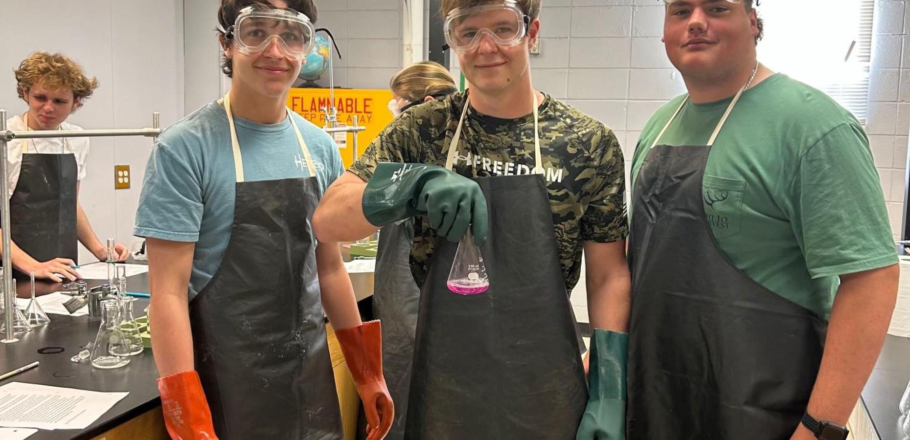 Three students in experiment gear hold a flask during a chemistry class.