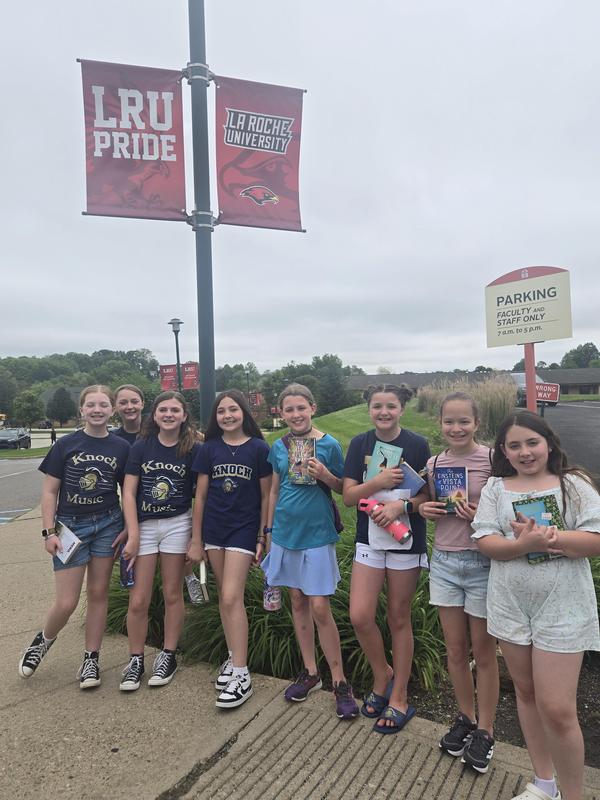 girls standing in a line holding books in front of Laroche flag