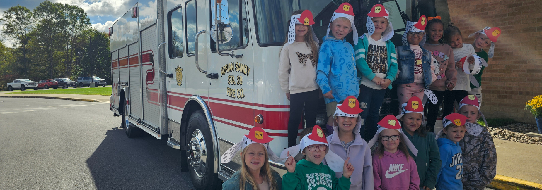 Group of children wearing firefighter hats in front of a fire truck.