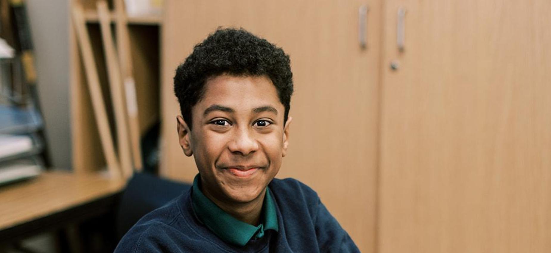 Smiling student in a navy sweater with an American flag sits at his desk