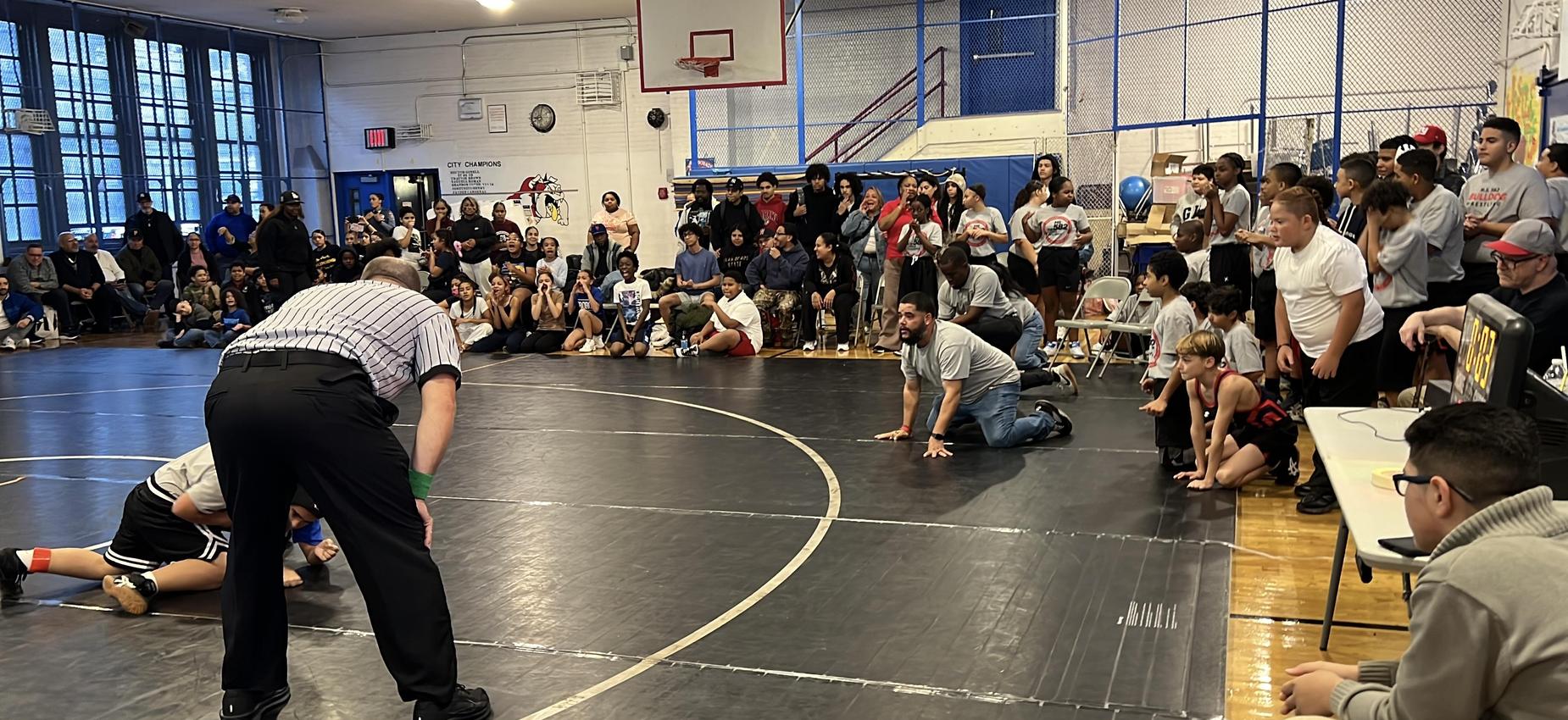 Wrestling Coach Betancourt fully engaged with his player on the mat.