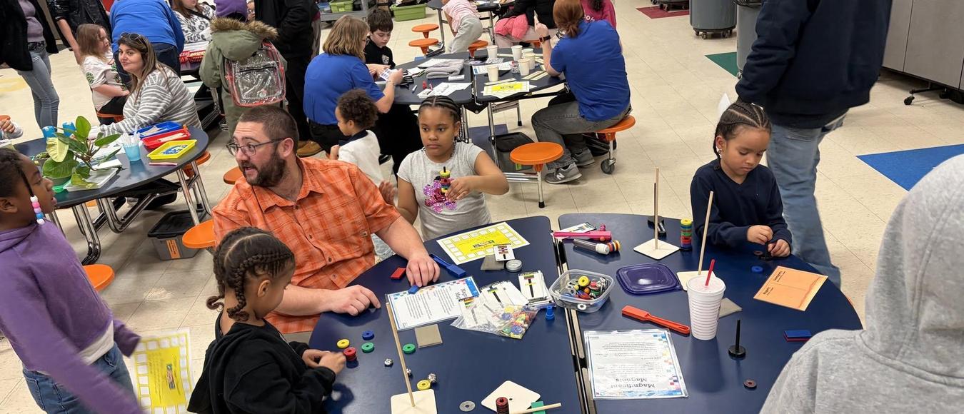 Families and students gather around blue tables for an interactive school science night event.