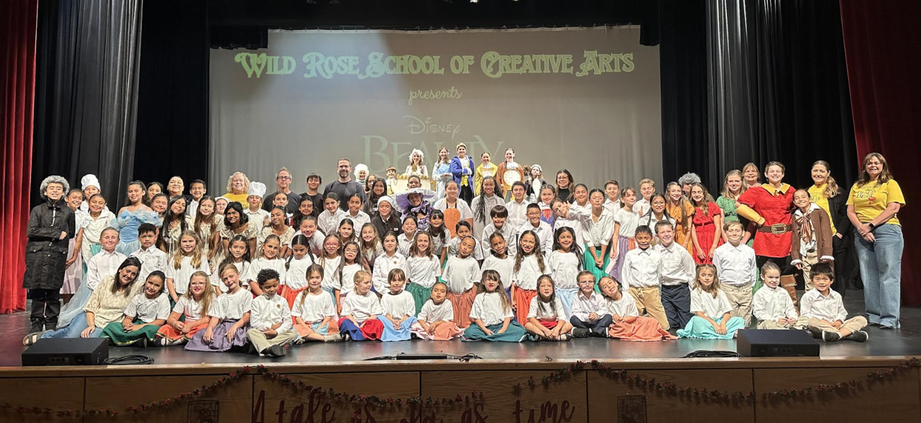 A large group of children and adults dressed in costumes posing on stage for a performance.