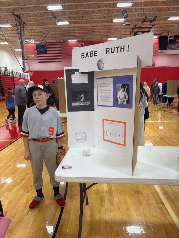 Boy in a baseball uniform presenting a project about Babe Ruth.