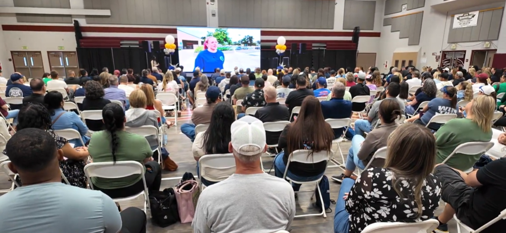 A large audience seated in a hall watching a presentation on a screen.