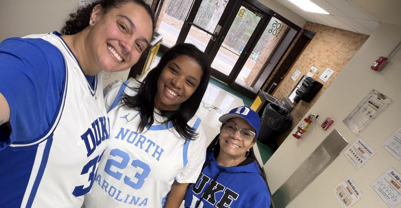 Three people smiling, wearing sports jerseys and hats, standing indoors.