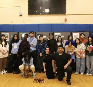 A group photo of diverse students and teachers posing in a gym with art displays.