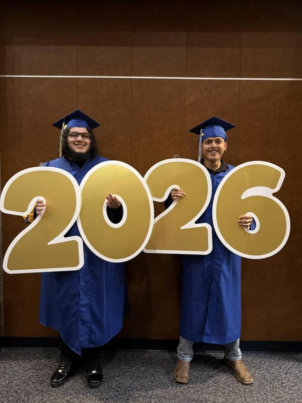 two Reese Education Center graduates in cap and gown posing with a 2026 sign