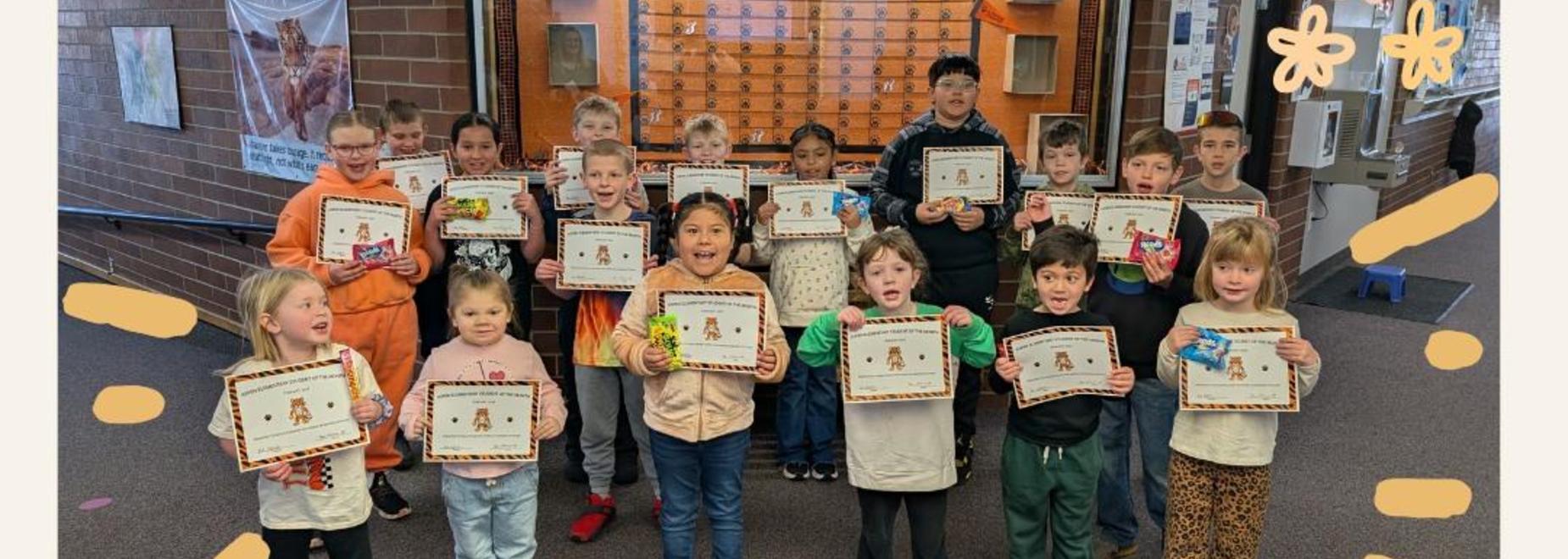 A group of children holding certificates and smiling in a school hallway.