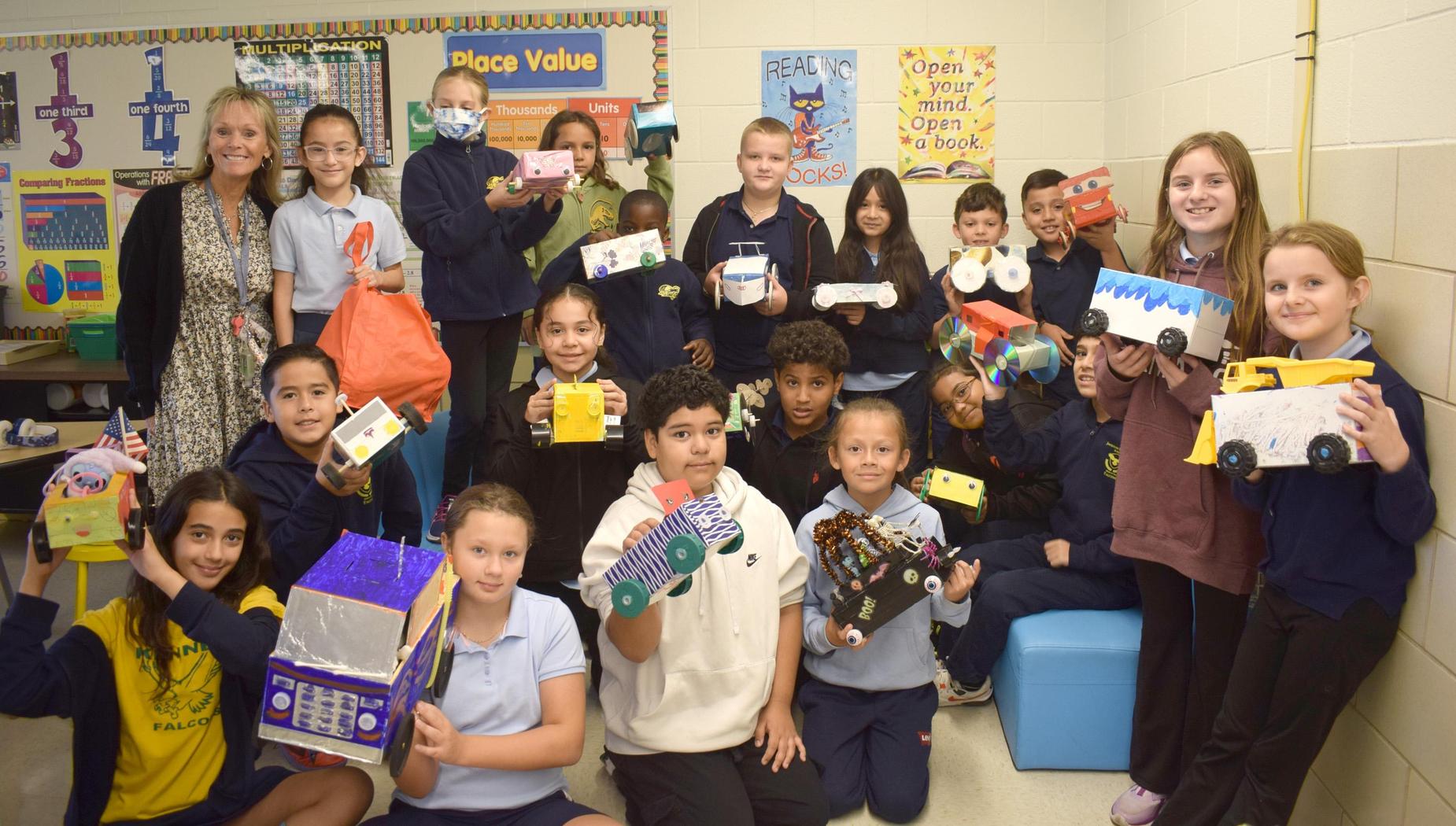 A group of students posing with their handmade toy cars in a classroom.