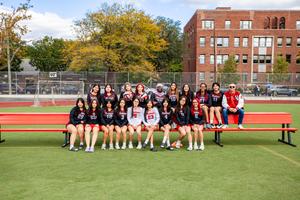 Newtown Varsity Volleyball team and their coach posing for a picture on a large bench on the Newtown Field.