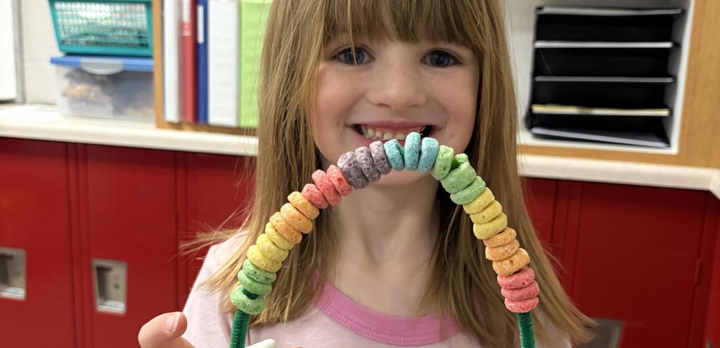 All smiles while holding a colorful cereal necklace.