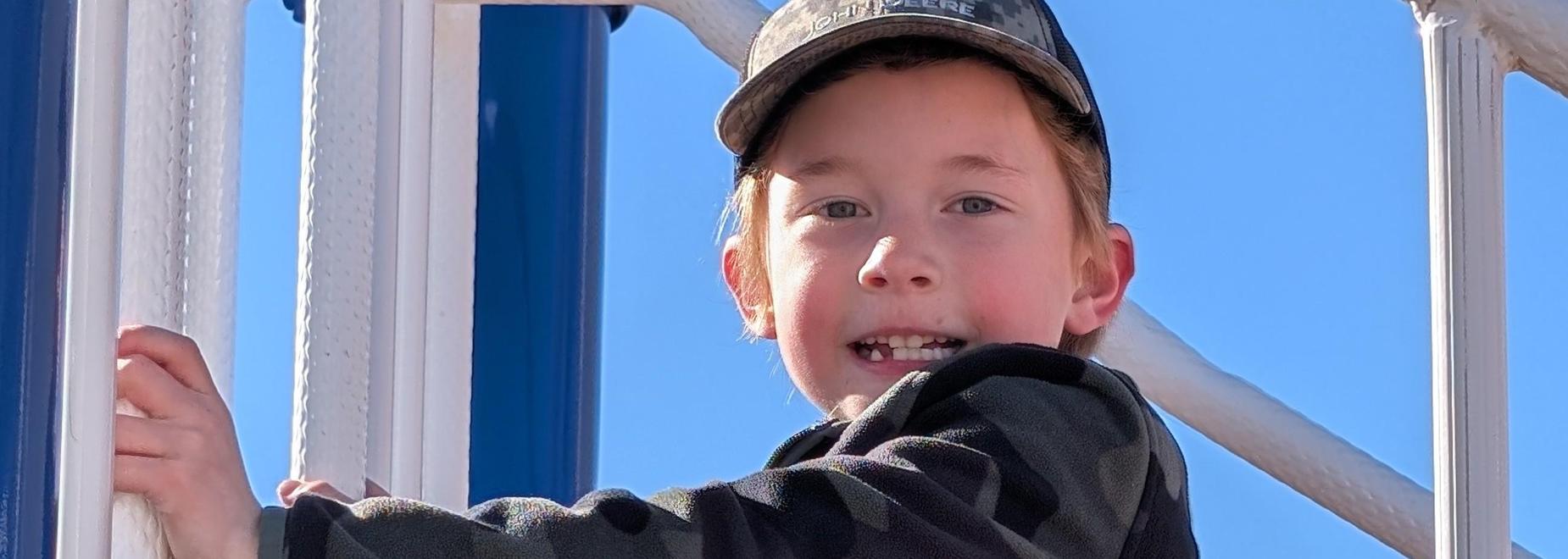 Child in camouflage hoodie climbing play equipment.