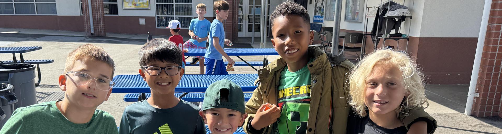 Group of five children smiling together outdoors, dressed in green and black clothing.
