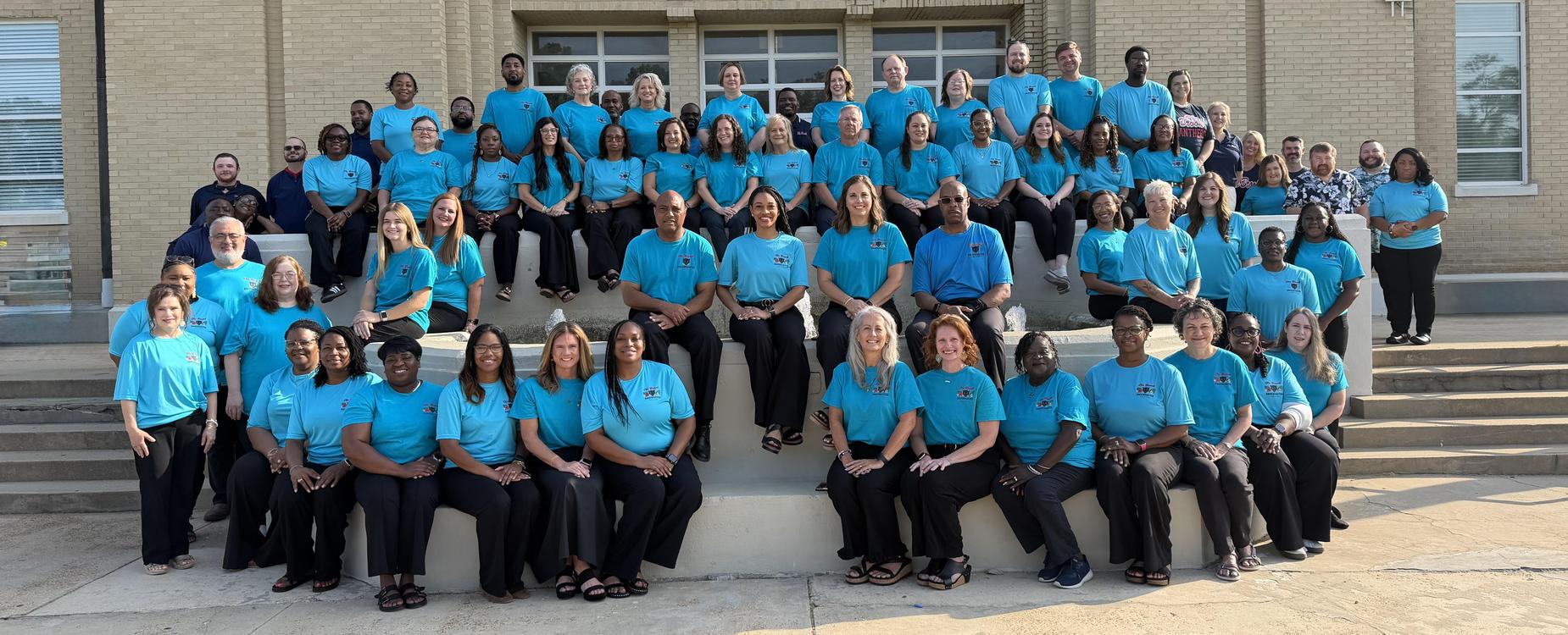 Large group of adults in matching blue shirts, posing on outdoor steps.