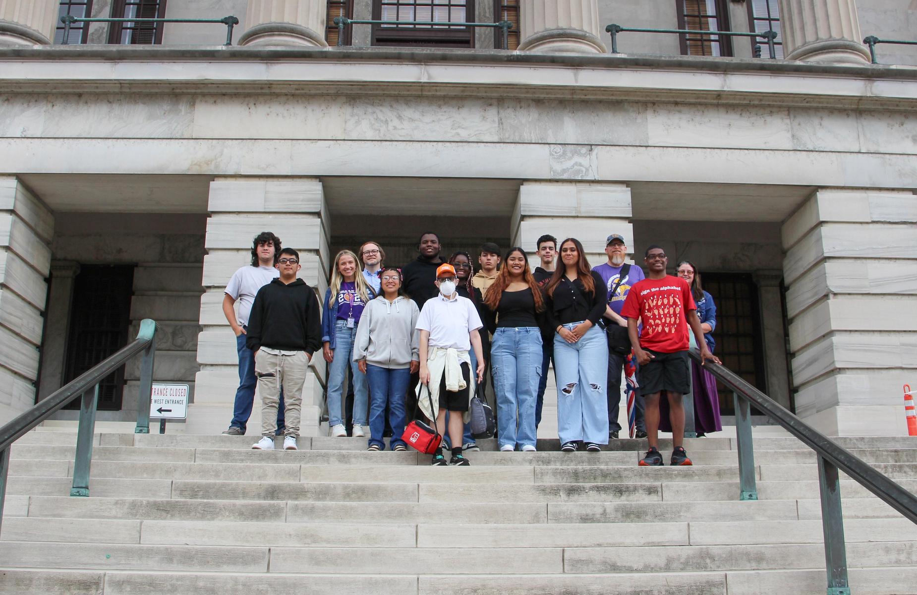 Group of diverse individuals posing together on outdoor stairs of a historic building.