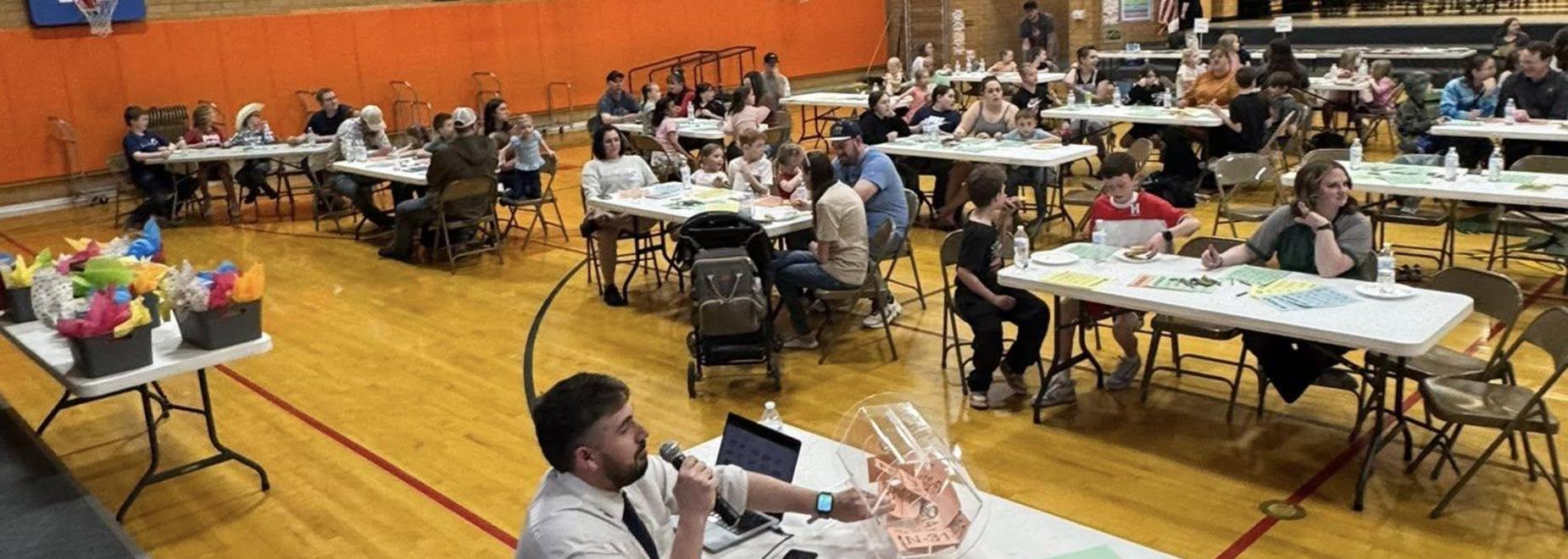 A large group of people sitting at tables in a gymnasium during an event.