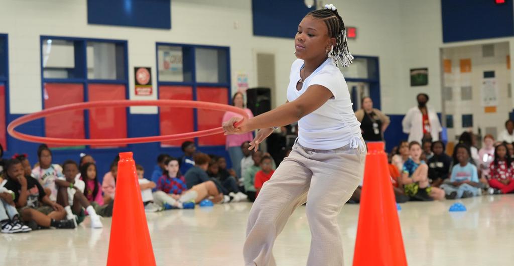 A girl tosses a hula hoop over a cone