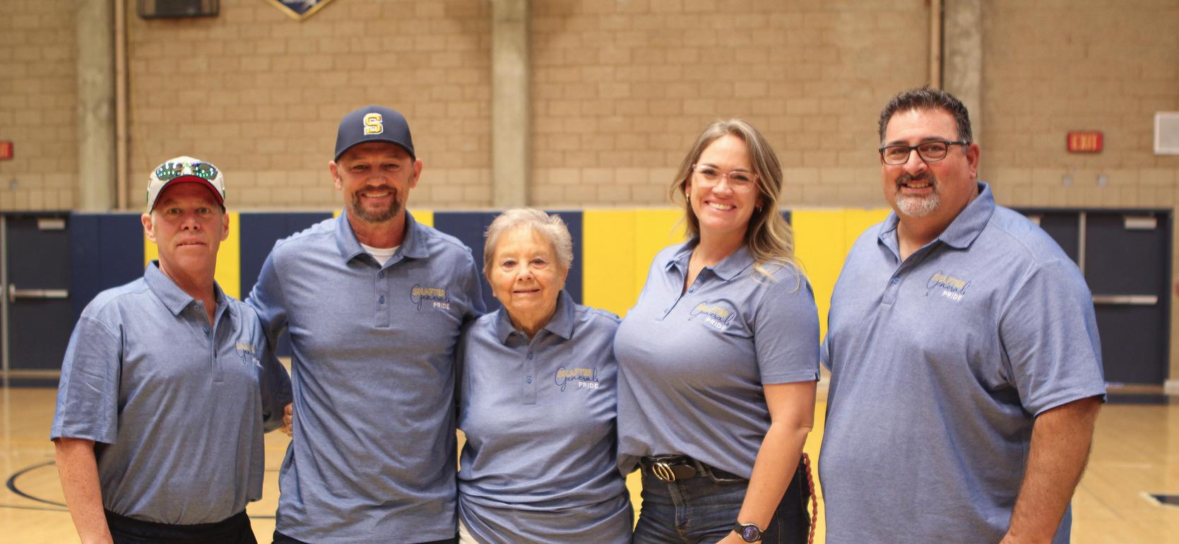 Five individuals in blue shirts posing together on a gym floor.