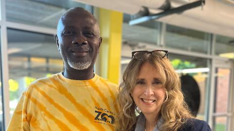 Smiling man in yellow tie-dye shirt standing beside a woman with wavy hair.