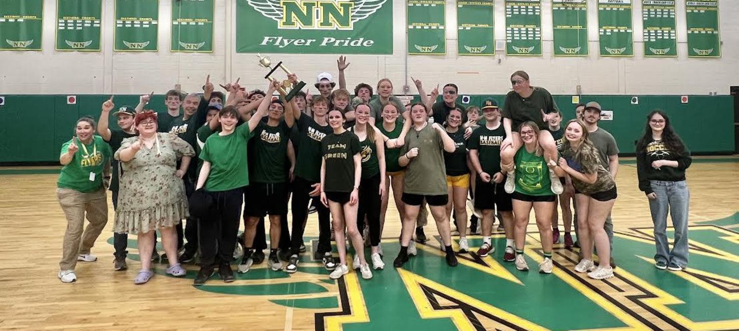 A group of students pose in a gym holding a trophy and celebrating