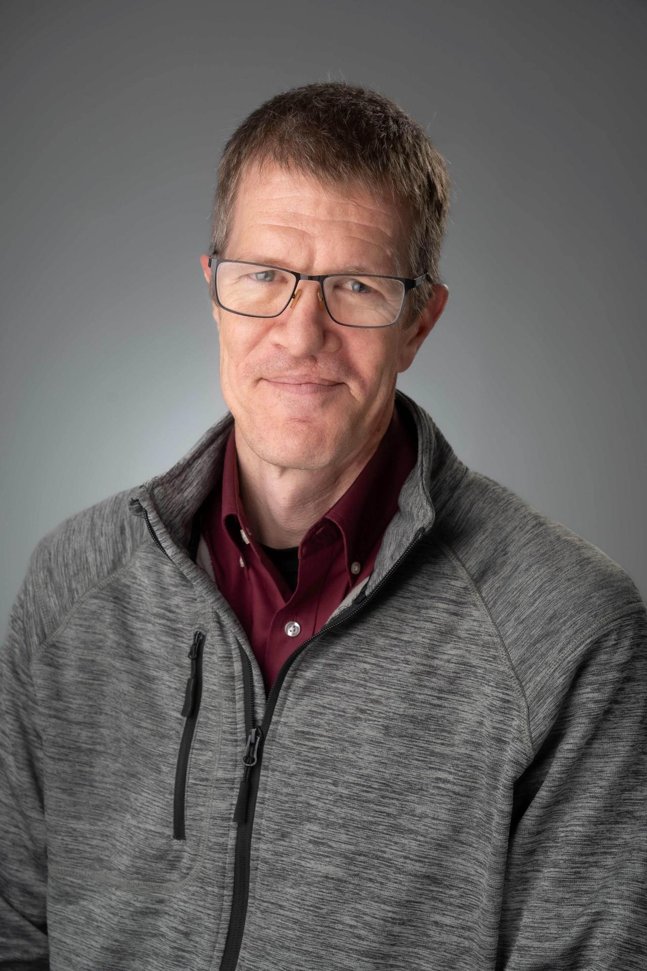 white male with glasses and close-cropped blonde hair in Burgundy shirt with gray sweater