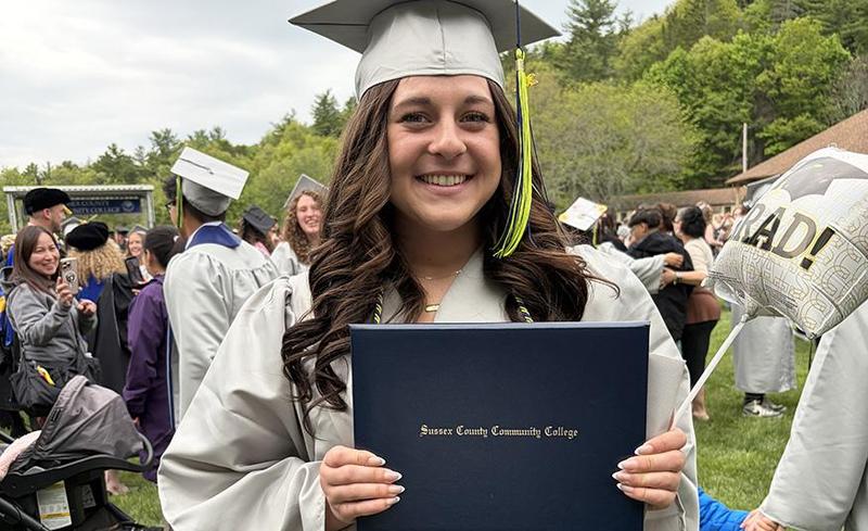 Aubrey White smiles in her graduation cap and gown while holding her diploma