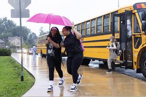 Two middle school students walk with an umbrella in rain