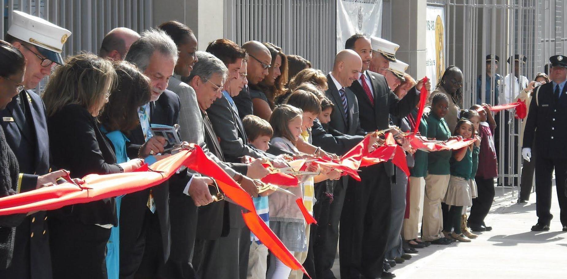 Group of adults and children participating in a ribbon-cutting ceremony.