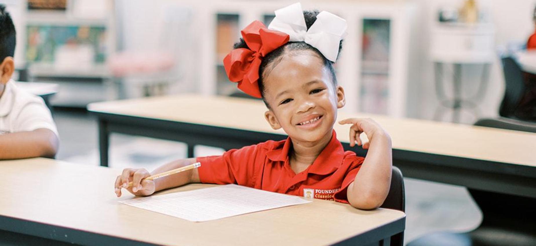 Smiling student with a red hair bow sitting at her desk