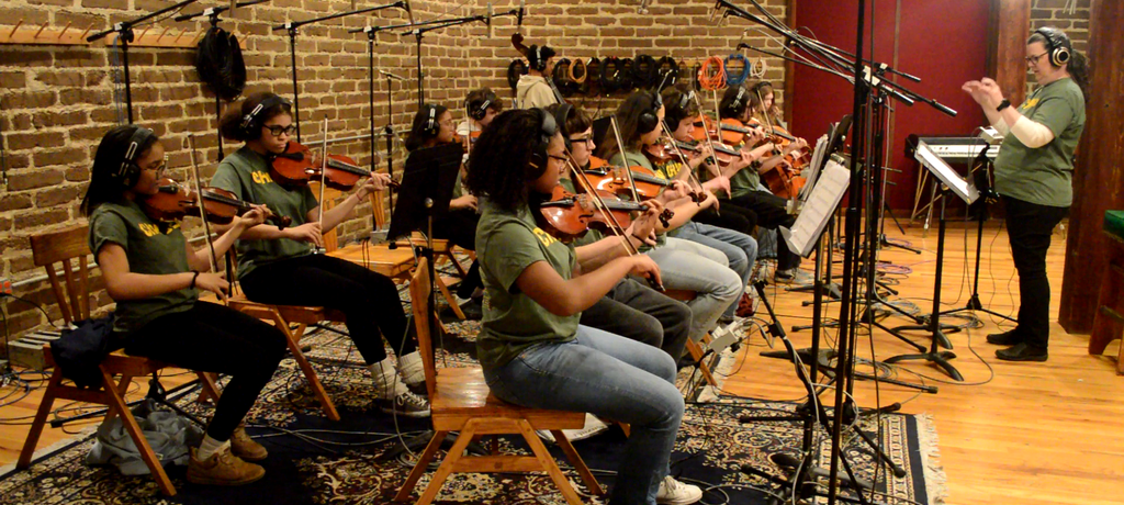 students wearing headphones and surrounded by microphones play stringed instruments