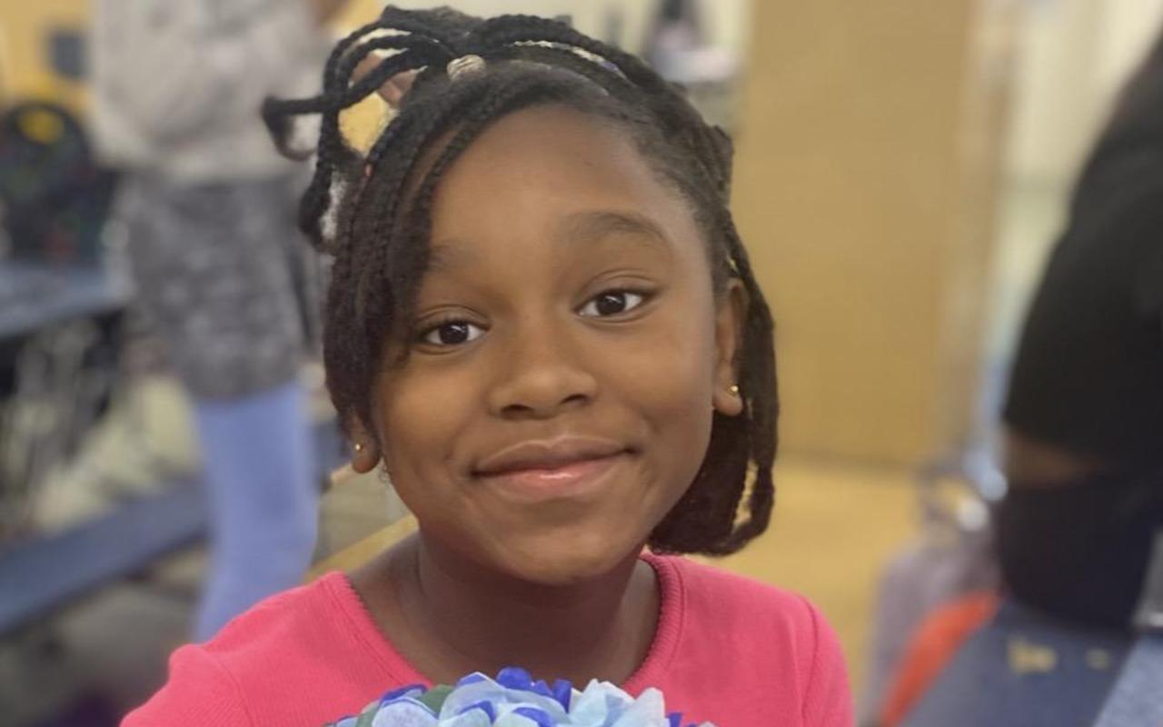 Girl holding a colorful paper flower, smiling at the camera.
