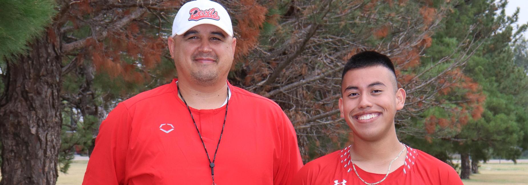 Coaches stand together in red jerseys on a grassy field.