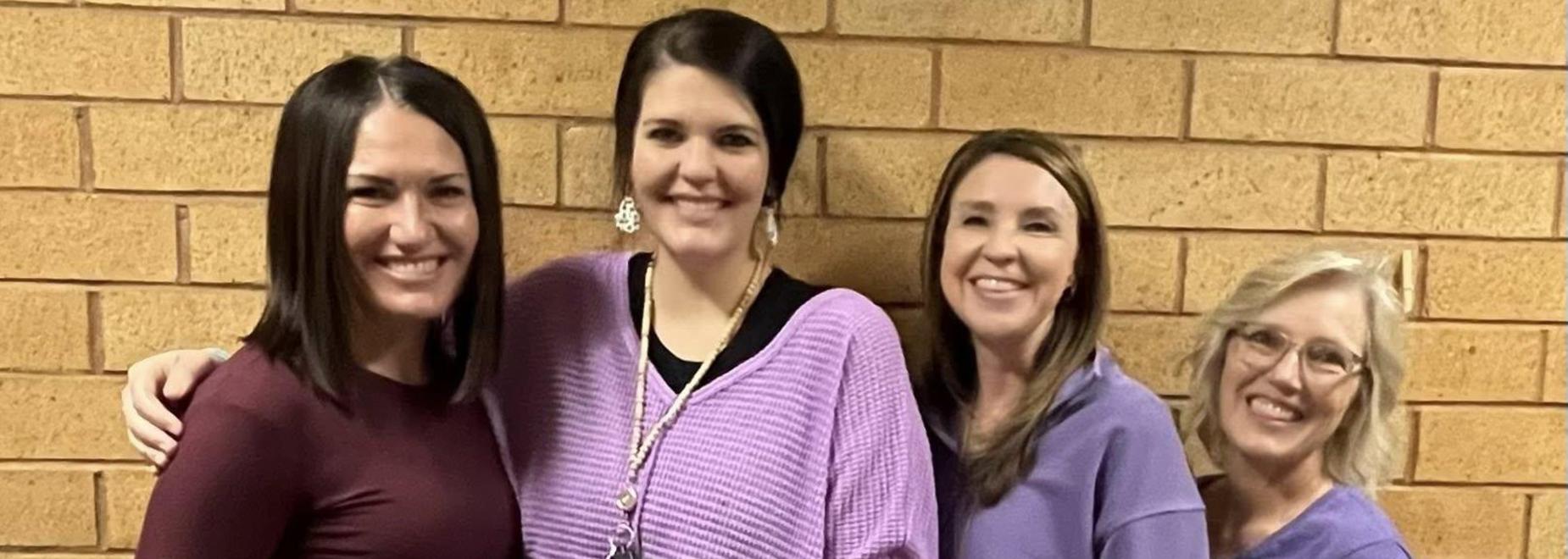 Four people posing together in casual outfits against a brick wall.