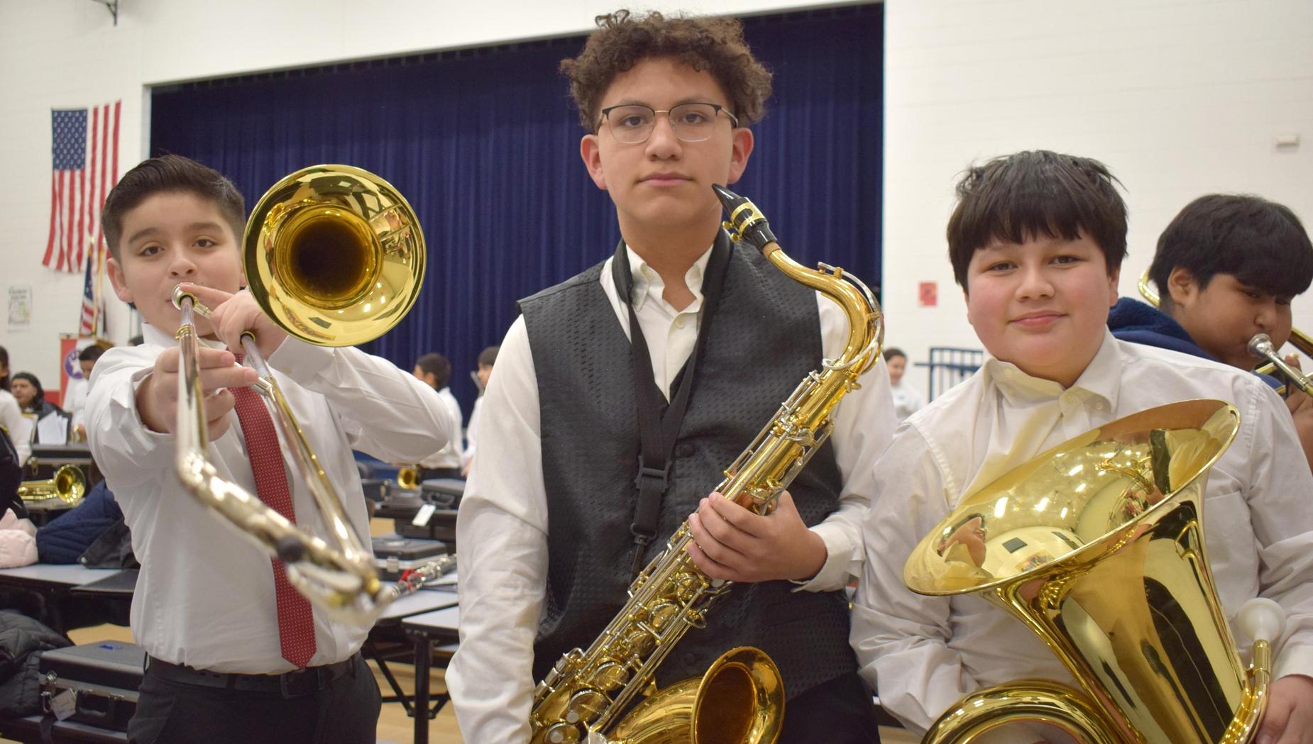 Three students posing with brass instruments, including a saxophone and trombones.