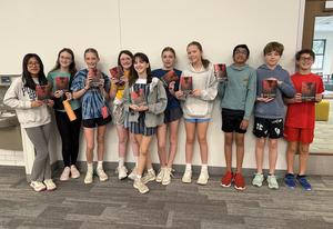 Group of kids holding books, smiling in a classroom setting.