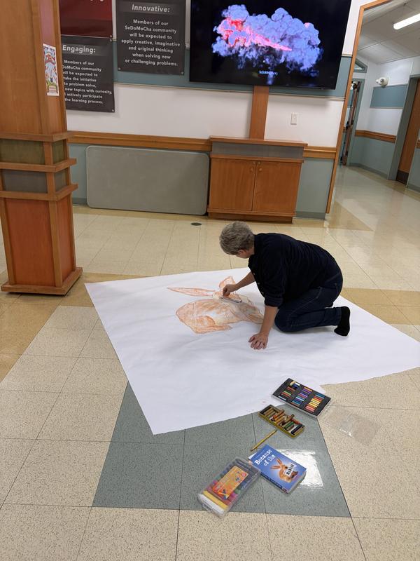 A person coloring on a large white sheet on the floor with pastels.