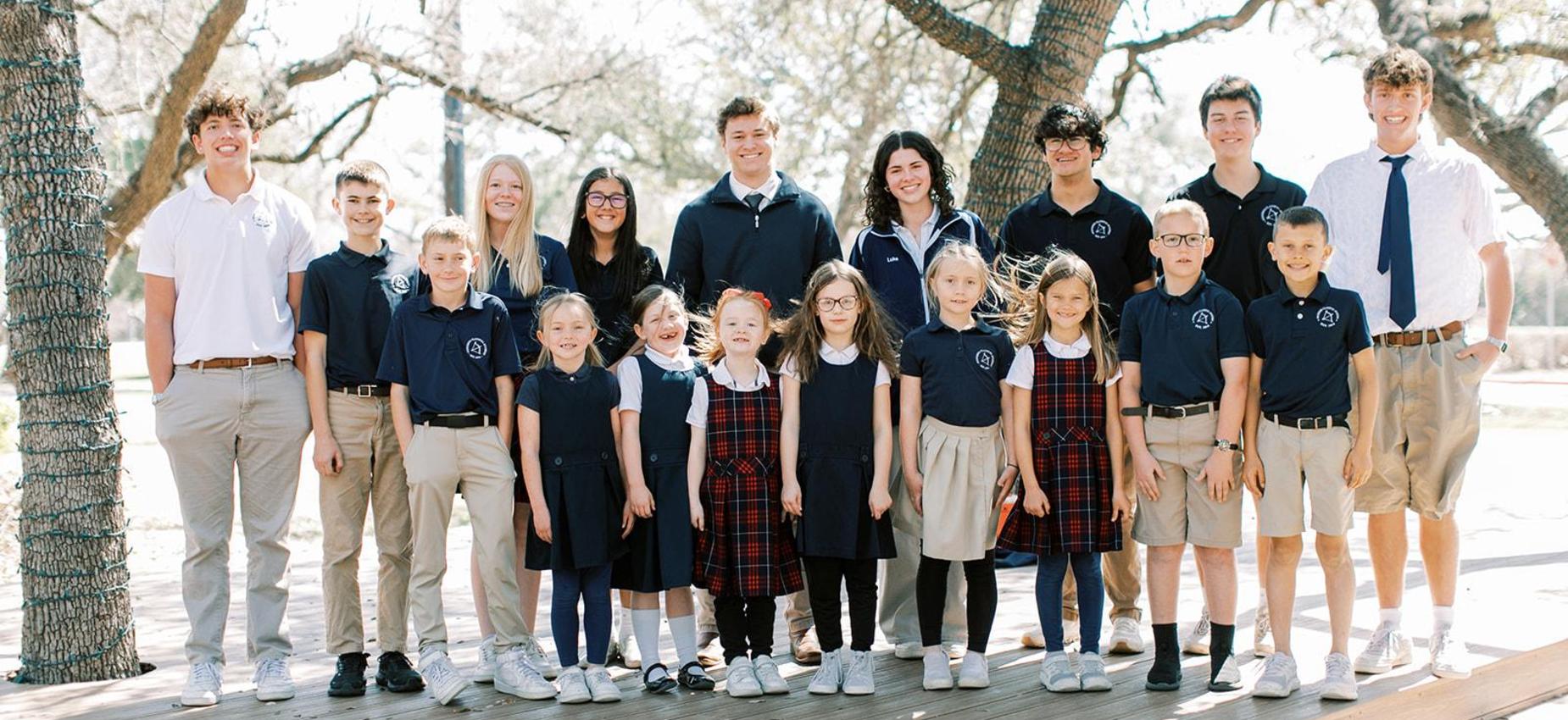 Students of all ages in Founders uniforms gather under oak trees