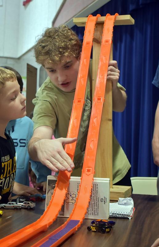 a boy standing behind a ramp for toy cars