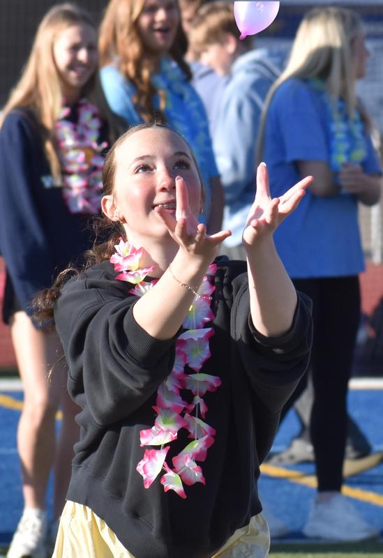 Girl in a black hoodie catches a balloon, surrounded by others wearing leis.