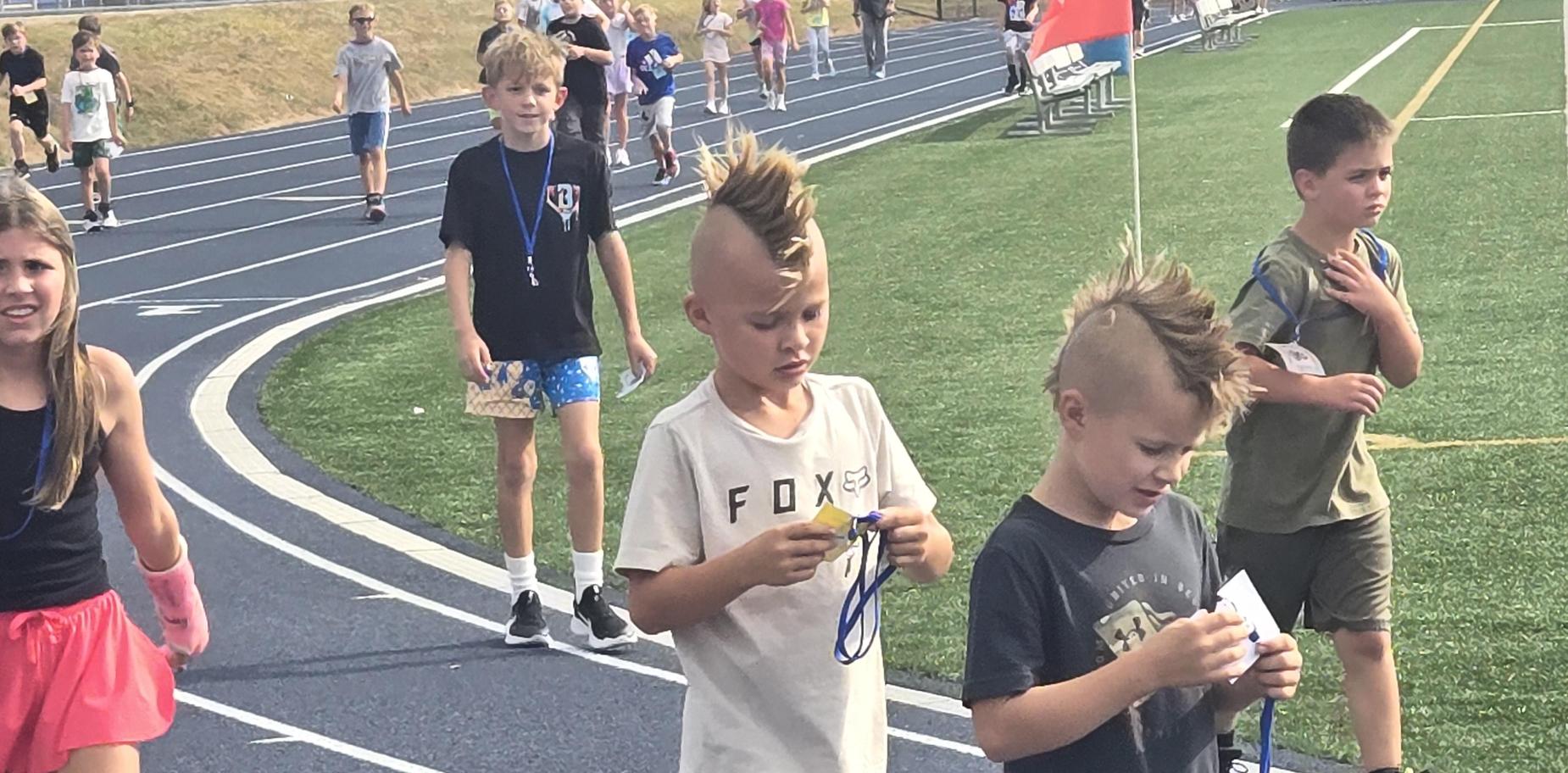 Kids with mohawks walking on a track, holding medals and showing excitement.