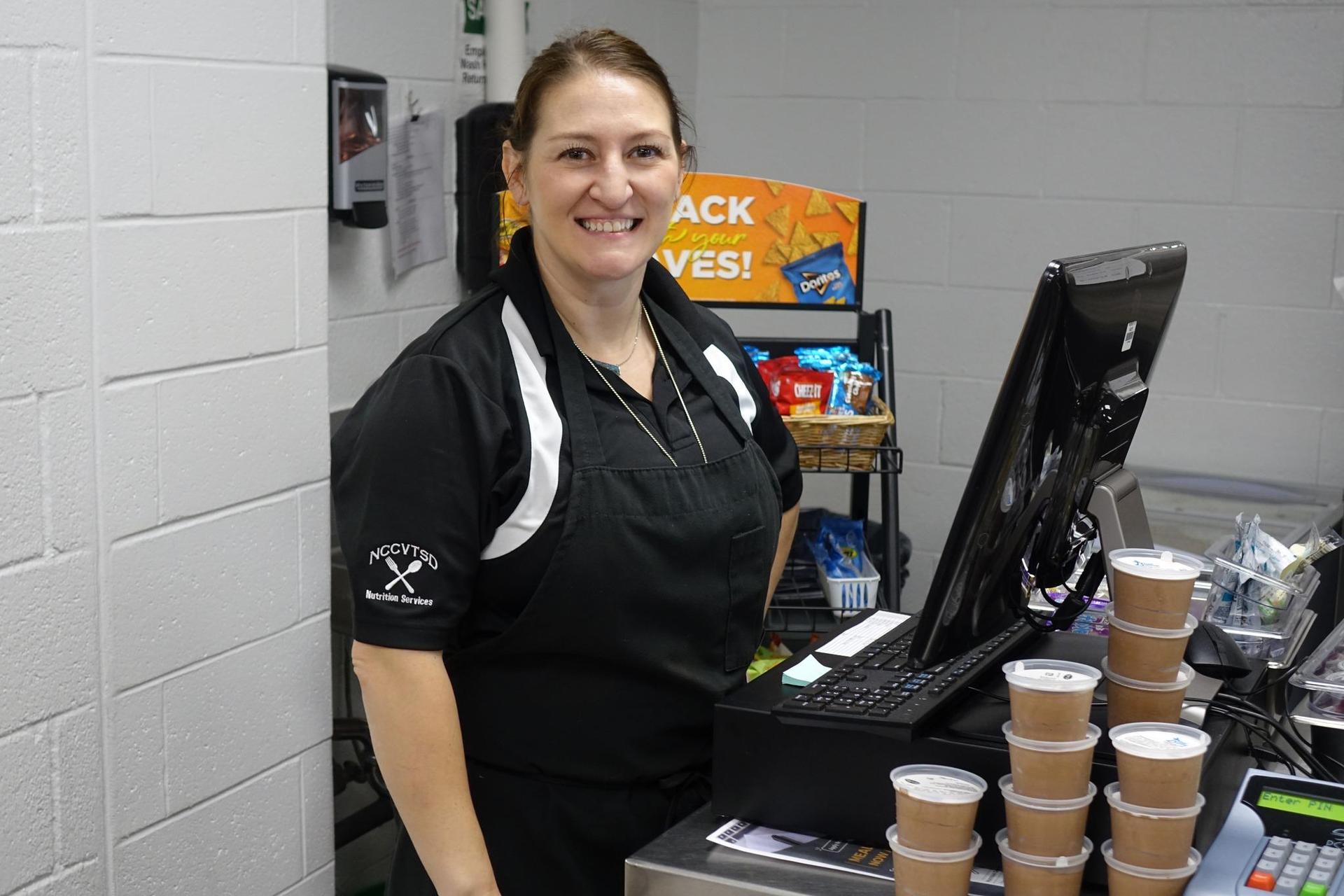 Smiling cashier stands behind a register with snacks behind her.