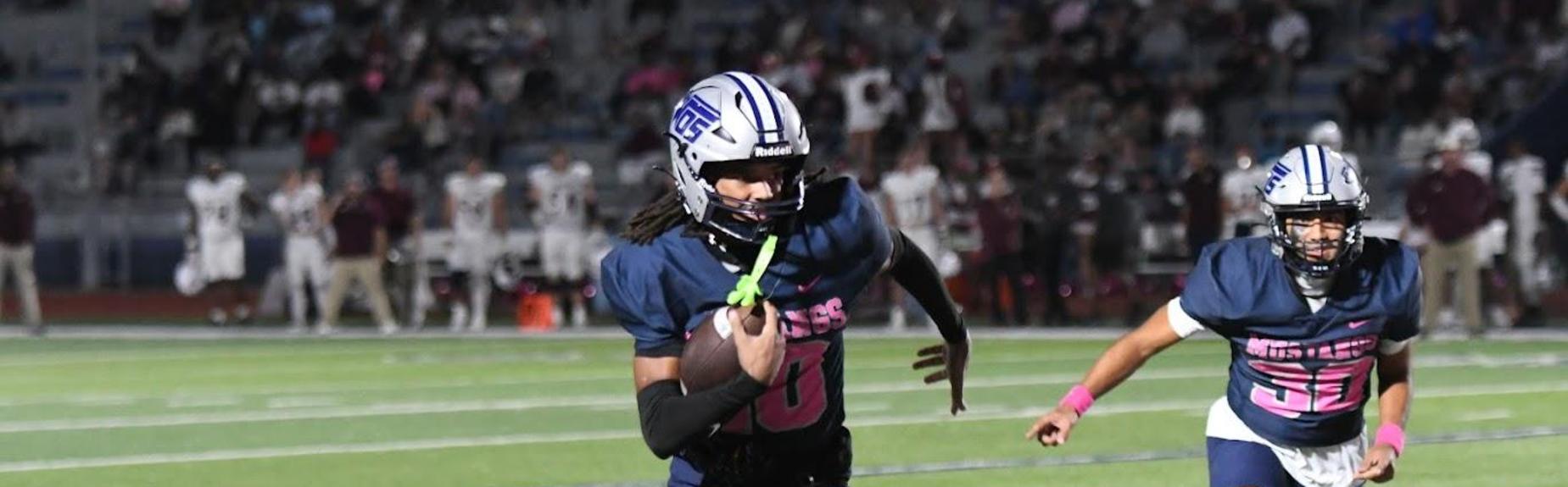 Football players in blue jerseys running on a field during a game.
